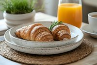 Fresh baked croissants with rosemary garnish served on ceramic plate with orange juice and coffee for continental breakfast morning meal setup.