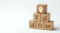 Wooden blocks with business icons stacked in pyramid formation showing lightbulb, dollar sign, growth chart, handshake and gear symbols on white background.