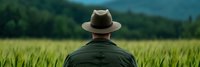 Farmer in hat standing in green wheat field looking at crop during growing season for agriculture and farming concept.