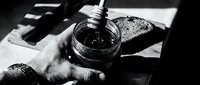 Young adult male hand holding open glass jar with dark liquid or substance, monochrome artistic composition with dramatic lighting and shadow, suitable for creative projects and editorial use.