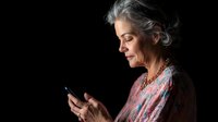 Senior woman with gray hair using smartphone against black background for technology and communication concepts.