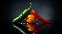 Fresh colorful chili peppers on dark reflective surface with dramatic lighting for culinary and cooking themes.