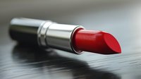 Vibrant red lipstick in metallic silver tube on dark wooden surface, perfect for beauty, cosmetics, and makeup artistry content.