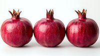 Fresh ripe pomegranates with glossy deep red skin and crown-like stems isolated on white background, ready for food and beverage design projects.