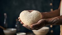 Elderly hands gently holding heart-shaped bread dough in warm kitchen lighting. Concept of love, care, baking, cooking and homemade food preparation.