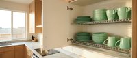 Modern kitchen cabinet interior with organized green dinnerware on wire shelving racks. Clean storage solution for plates, bowls and mugs in contemporary home.