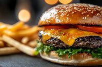 Juicy cheeseburger with melted cheddar, fresh lettuce, tomato on sesame seed bun served with golden french fries. Close up view with bokeh background.