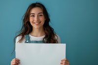 Young Asian woman with natural makeup and wavy brown hair holding blank white poster against turquoise wall. Perfect for advertising, social media campaigns and mockup designs.