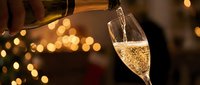Champagne being poured into a flute glass with golden bokeh lights in background, suitable for celebration, holiday, and festive event marketing materials.