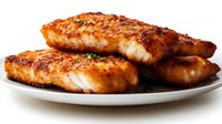 Crispy pan-seared fish fillets with golden-brown crust and herbs served on white plate, close up view showing flaky texture and seasoned exterior.