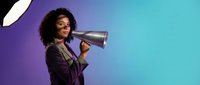Young African American businesswoman with curly hair speaking through megaphone on vibrant purple and teal gradient background for marketing campaigns.