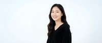 Young Asian businesswoman in black blazer smiling confidently against white background for professional headshot and corporate marketing materials.