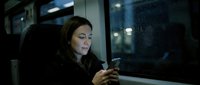 Young woman of mixed ethnicity using smartphone on public transport at night, urban commuting and mobile technology concept.