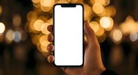 Hand holding smartphone with blank white screen against warm bokeh lights background for app mockup and digital display presentations.