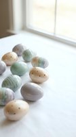 Pastel colored Easter eggs with speckled and marbled patterns scattered on white surface near bright window for spring holiday celebration and decoration.
