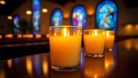 Glowing prayer candles in glass holders against colorful stained glass windows in church, creating peaceful spiritual atmosphere.