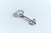 Vintage silver key with ornate crown-shaped bow lying on white background, isolated object for design projects and security concepts.