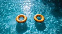 Yellow inflatable rings floating on rippling turquoise pool water with sun reflections creating dynamic light patterns on swimming pool surface.