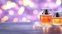 Luxury perfume bottles with amber fragrance on reflective surface against purple bokeh background with sparkly fairy lights creating romantic atmosphere.