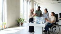 Diverse business team collaborating in modern office with wheelchair accessibility, promoting inclusive workplace culture and teamwork among professionals.