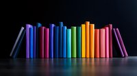 Row of colorful hardcover books arranged in rainbow spectrum order standing on dark surface against black background, creating vibrant minimalist composition.