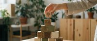 Hand placing wooden cube on pyramid stack representing business growth strategy and goal achievement in modern office environment.