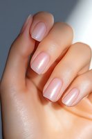 Close-up of elegant manicured nails featuring soft pink pearl shimmer polish on natural-looking nails against neutral background, showcasing modern nail art trends.