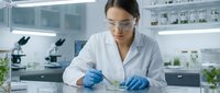 Female scientist in white lab coat and safety glasses conducting research with test tube in modern laboratory setting for scientific studies.