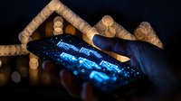 Glowing smartphone screen illuminated at night with bokeh lights background, hand holding mobile device displaying bright blue digital interface.