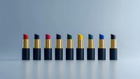 Row of colorful luxury lipsticks in black tubes arranged in minimalist composition against gray background, showcasing variety of trendy shades for cosmetics marketing.