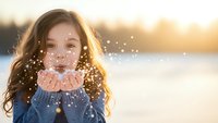 Young woman blowing glitter confetti from hands during golden hour sunset creating magical sparkles in winter outdoor portrait for celebration concepts.