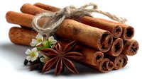 Aromatic cinnamon sticks tied with rustic twine, accompanied by star anise and delicate white flowers on white background.