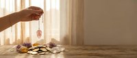 Hand holding crystal pendulum over wooden table with healing stones and crystals for spiritual divination meditation and energy work session.