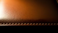 Brown leather texture with decorative stitching detail for luxury goods, fashion accessories, upholstery and premium material backgrounds.