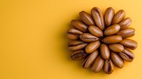 Roasted pecan nuts arranged in circular pattern on vibrant yellow background. Minimalist food photography with copy space for healthy eating concept.