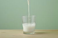 Fresh milk pouring into clear glass creating splash and foam on wooden table against mint green background, dairy drink photography.
