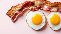 Crispy fried bacon strips and sunny side up eggs with bright yellow yolks on white background, classic breakfast combination for menu and food service.
