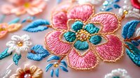 Colorful floral embroidery with pink and teal flowers featuring detailed stitchwork and golden accents on light fabric, showcasing traditional needlework technique.