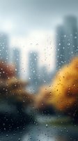 Raindrops on window glass with blurred urban cityscape background showing skyscrapers and autumn trees creating moody atmospheric scene in soft focus.