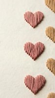 Handmade embroidered hearts in pink and beige thread on cream fabric background for Valentine's Day crafts and romantic textile projects.