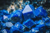 Vibrant blue crystal formation with geometric shapes and facets in natural mineral cluster, macro photography showing detailed crystalline structure and light reflections.