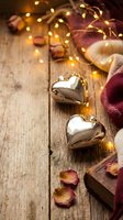 Golden heart ornaments with warm fairy lights, chocolate and rose petals on rustic wooden background for romantic Valentine's Day celebration.