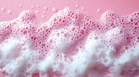Pink foam bubbles with white soap suds creating abstract wave pattern on pink background, macro photography showing detailed texture of cleaning product.