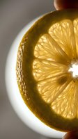 Backlit lemon slice showing translucent yellow flesh and detailed segment structure, held against bright light for beverage, culinary, and food styling applications.