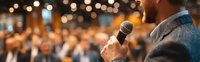 Professional speaker addressing audience at corporate conference with microphone and warm ambient lighting for business presentations.
