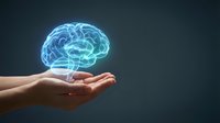 Glowing blue brain hologram floating above open human hands against dark background representing artificial intelligence and mental health concepts.