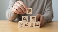 Business professional arranging wooden blocks with strategy icons including target, gears, lightbulb and charts for corporate planning and goal achievement.