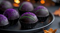 Dark chocolate truffles decorated with purple sugar sprinkles on black plate. Elegant dessert with autumn maple leaf and bokeh lights create luxurious mood.