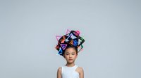 Young Asian girl wearing colorful geometric paper crowns on her head against neutral background, suitable for creative, educational, and children's design projects.