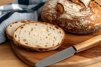 Freshly baked artisan sourdough bread with crispy crust sliced on wooden cutting board, showing airy crumb texture and served with bread knife.